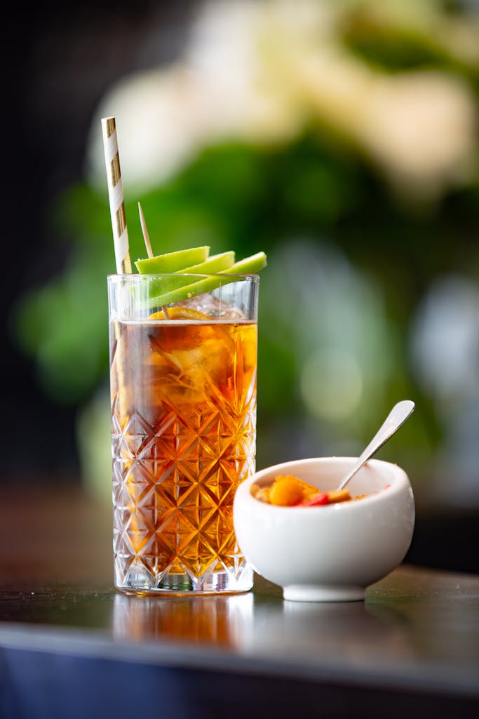 Refreshing iced tea with green apple garnish beside a bowl of colorful fruits.