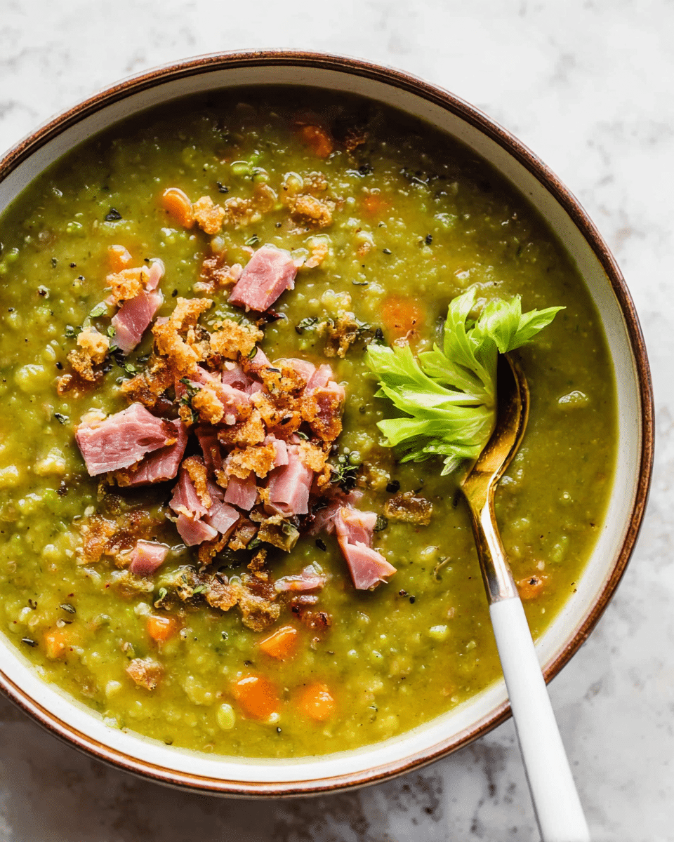 The image shows a white bowl with a brown rim filled with thick green pea soup mixed with small orange carrot pieces and bits of herbs throughout. On top, there are scattered chunks of pink ham and a sprinkle of crispy, crumbled toppings with a light beige color. Two bright green celery leaves rest on the surface near the center. A gold spoon with a white handle is partially submerged on the right side of the bowl, resting on the soup. The background has a white marbled texture. photo taken with an iphone --ar 4:5 --v 7