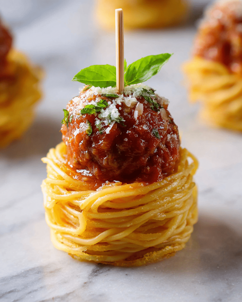 A small nest of golden yellow spaghetti forms the first layer at the bottom, tightly wound into a circular shape. On top of the pasta rests a round, textured brown meatball coated in a rich red tomato sauce. The meatball is sprinkled with fine white grated cheese, adding a light contrast. A small green basil leaf is placed vertically on top, attached to a thin wooden skewer piercing through all layers. The dish is set on a white marbled surface. photo taken with an iphone --ar 4:5 --v 7