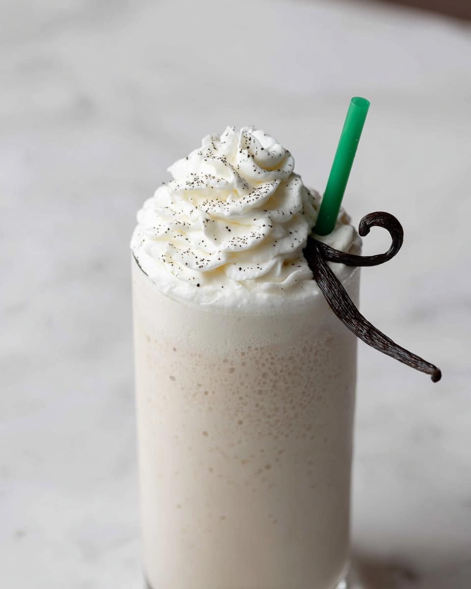 The image shows a tall glass filled with a creamy, light beige milkshake. On top, there is a thick layer of white whipped cream with small black specks sprinkled over it. A dark brown vanilla bean pod curls gently over the whipped cream, adding contrast. A green straw is inserted into the drink on the right side. The glass is placed on a surface with a white marbled texture. photo taken with an iphone --ar 4:5 --v 7