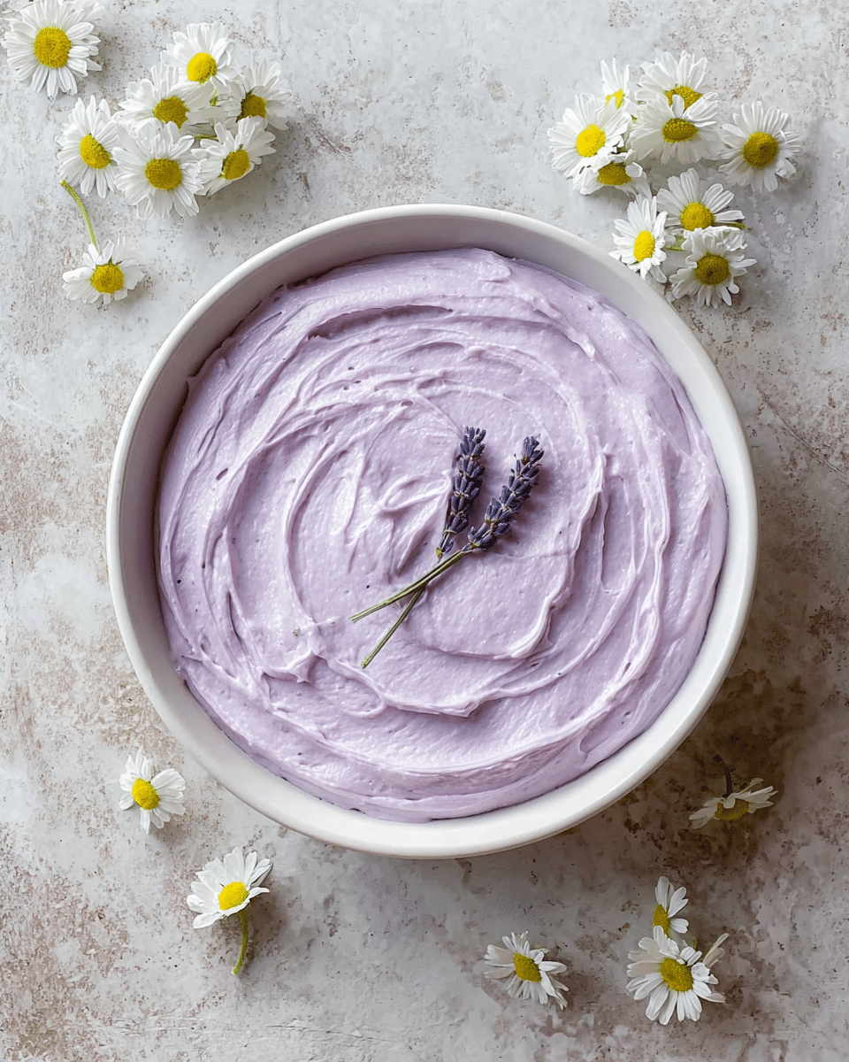 A single-layer dessert with a smooth, thick spread of light purple cream filling a round white bowl, textured with gentle swirls that create soft waves on the surface; two small sprigs of lavender rest neatly in the center, adding a delicate touch; the bowl sits on a white marbled texture surface, surrounded by scattered small white daisies with yellow centers that provide a fresh, natural feel. photo taken with an iphone --ar 4:5 --v 7
