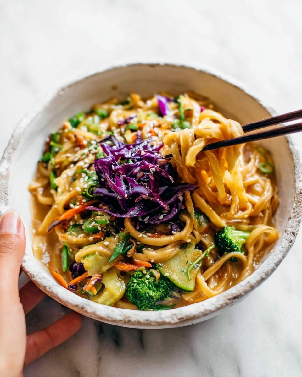 A bowl filled with thick noodles covered in a light brown sauce sits on a white marbled surface. The noodles are mixed with bright green broccoli pieces, orange shredded carrots, and bits of light green zucchini, all topped with a small pile of dark purple shredded cabbage in the center. The dish is sprinkled lightly with white sesame seeds. A woman's hand holding dark chopsticks lifts a clump of noodles from the bowl. The bowl is white with a rough, natural texture resembling stone. Photo taken with an iphone --ar 4:5 --v 7
