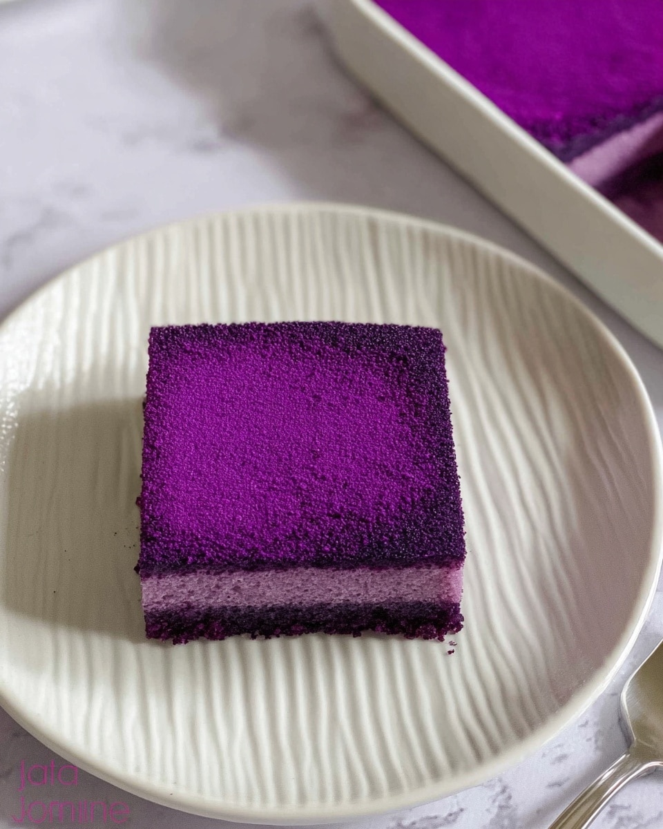 A small square piece of cake with a smooth, bright purple top layer dusted evenly, showing a rich and velvety texture. The cake sits alone in the center of a white plate with subtle vertical ridges along the edges. Around the cake, the edges are slightly crumbly with deep purple crumbs, hinting at a soft inside. In the upper right corner, a white rectangular dish filled with more of the same bright purple cake is visible. The background is a white marbled texture, and a silver fork lies to the right side of the plate. photo taken with an iphone --ar 4:5 --v 7