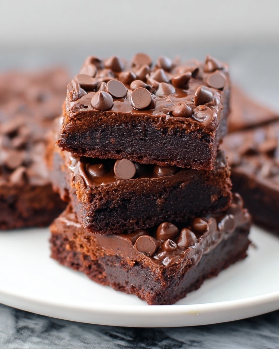 A white plate holds a stack of five square chocolate brownies with three visible layers: a rich, dark brown bottom layer that looks dense and fudgy, a slightly lighter middle layer made of moist chocolate cake, and a top layer covered in smooth, shiny chocolate frosting scattered generously with milk chocolate chips. The brownies are placed on a white marbled surface, and the close-up view highlights the textures of the chocolate chips and the moist cake underneath. Photo taken with an iphone --ar 4:5 --v 7