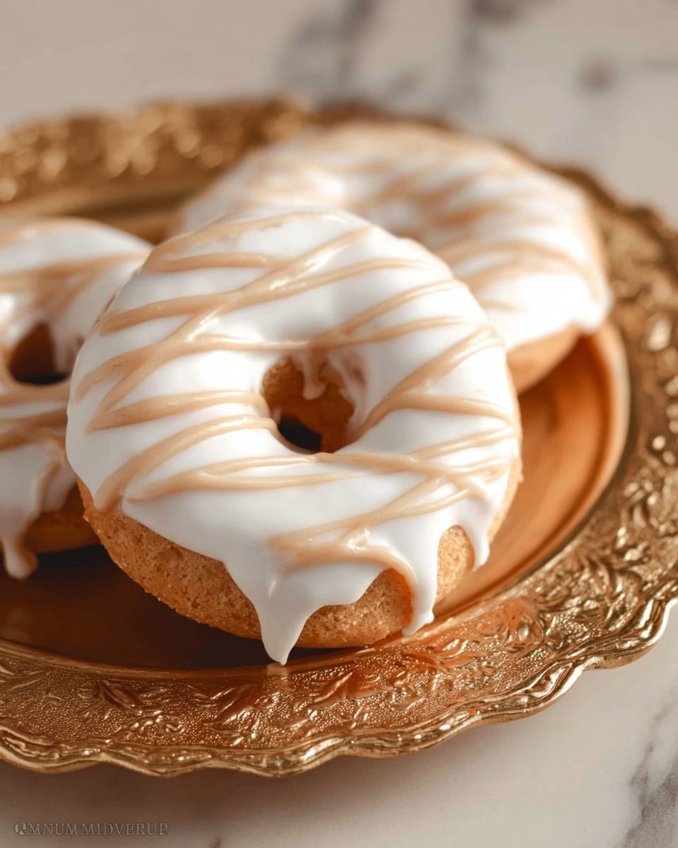 The image shows three freshly baked donuts on an ornate gold tray with a detailed edge. Each donut has a thick white icing layer covering the top, with smooth texture, and light brown glaze lines drizzled over it in a diagonal pattern. The donuts are a golden brown color beneath the icing, soft and fluffy in appearance. The background is a white marbled texture that softly reflects light, giving an elegant and clean look to the setting. photo taken with an iphone --ar 4:5 --v 7