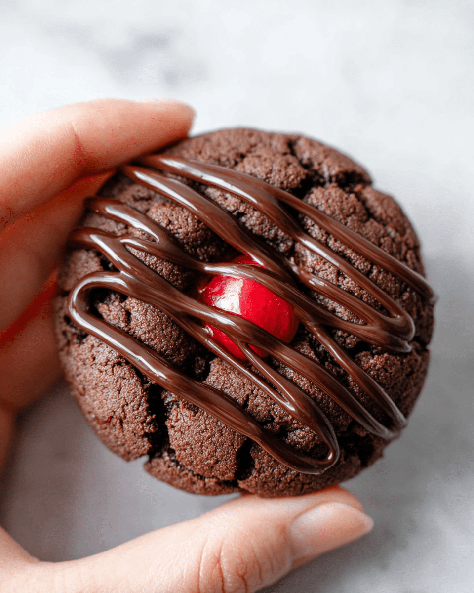 A close-up image shows a single dark brown chocolate cookie with a rough cracked texture. On top, there are five thick, smooth lines of shiny chocolate drizzle arranged diagonally, covering the cookie from left to right. In the center, there is a bright red glossy cherry partially wrapped by some of the chocolate drizzle. A woman's hand with visible skin texture holds the cookie gently at the bottom right edge. The background is a white marbled surface. photo taken with an iphone --ar 4:5 --v 7