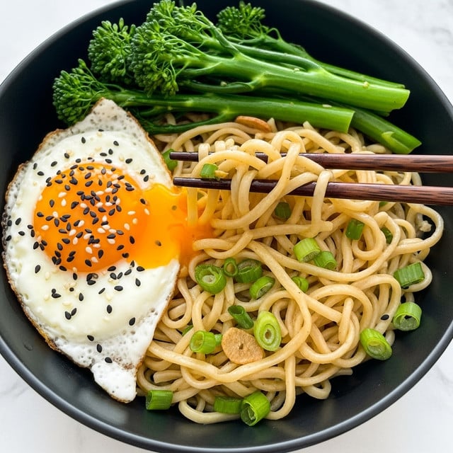 The image shows a black bowl filled with three main parts layered side by side: light yellow cooked noodles mixed with small green onion pieces in the front and right, bright green cooked broccolini at the back, and a sunny-side-up egg on the left with a white edge and a runny, vibrant orange yolk topped with black sesame seeds. Dark brown chopsticks are picking up some noodles from the right side of the bowl. The bowl is placed on a white marbled surface. photo taken with an iphone --ar 4:5 --v 7