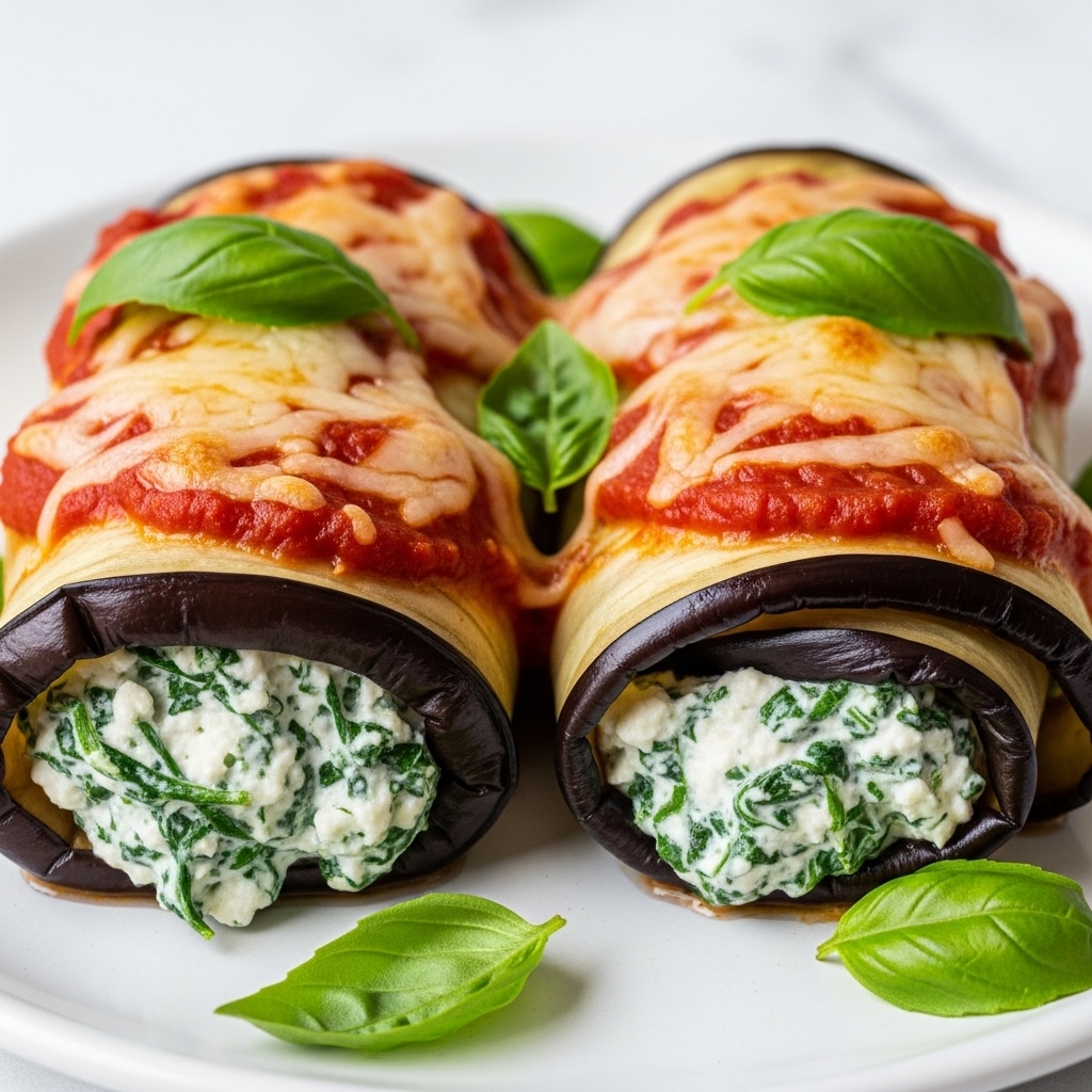 A close-up of two rolled eggplant slices filled with a creamy white cheese mixed with finely chopped green spinach, placed side by side on a white plate with a white marbled texture background; the eggplant skin is deep purple with a smooth, shiny surface, and inside the filling is slightly browned from baking. Each roll is topped with layers of bright red tomato sauce and melted golden-brown cheese, garnished with fresh green basil leaves on top and around the rolls. The rich textures of the soft cheese filling, the tender eggplant, and bubbling sauce create a warm and inviting look. Photo taken with an iphone --ar 4:5 --v 7