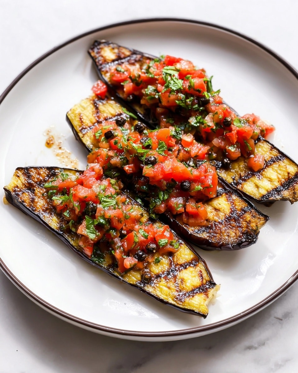 The dish shows four pieces of grilled eggplant slices arranged on a white plate with a thin dark rim. Each eggplant slice is cut lengthwise and has a golden brown, slightly charred, crisscross pattern on the surface. On top of each slice, there is a topping made of finely chopped bright red tomatoes mixed with green herbs and small dark peppercorns scattered throughout. The plate sits on a white marbled surface, and the lighting highlights the glossy texture of the grilled eggplant and fresh topping. photo taken with an iphone --ar 4:5 --v 7