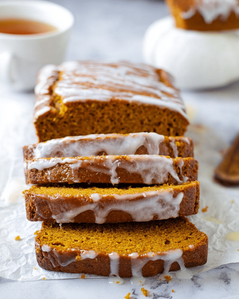 The image shows a loaf of pumpkin bread sliced into five thick pieces, arranged in a slightly staggered stack. The pumpkin bread has a soft texture with small air holes and a warm brown-orange color. The top layer is glossy and lightly drizzled with a thin layer of white glaze that drips down the sides, adding a shiny contrast. The bread sits on white parchment paper against a white marbled surface. In the background, there is a white cup filled with tea, slightly out of focus. Photo taken with an iphone --ar 4:5 --v 7