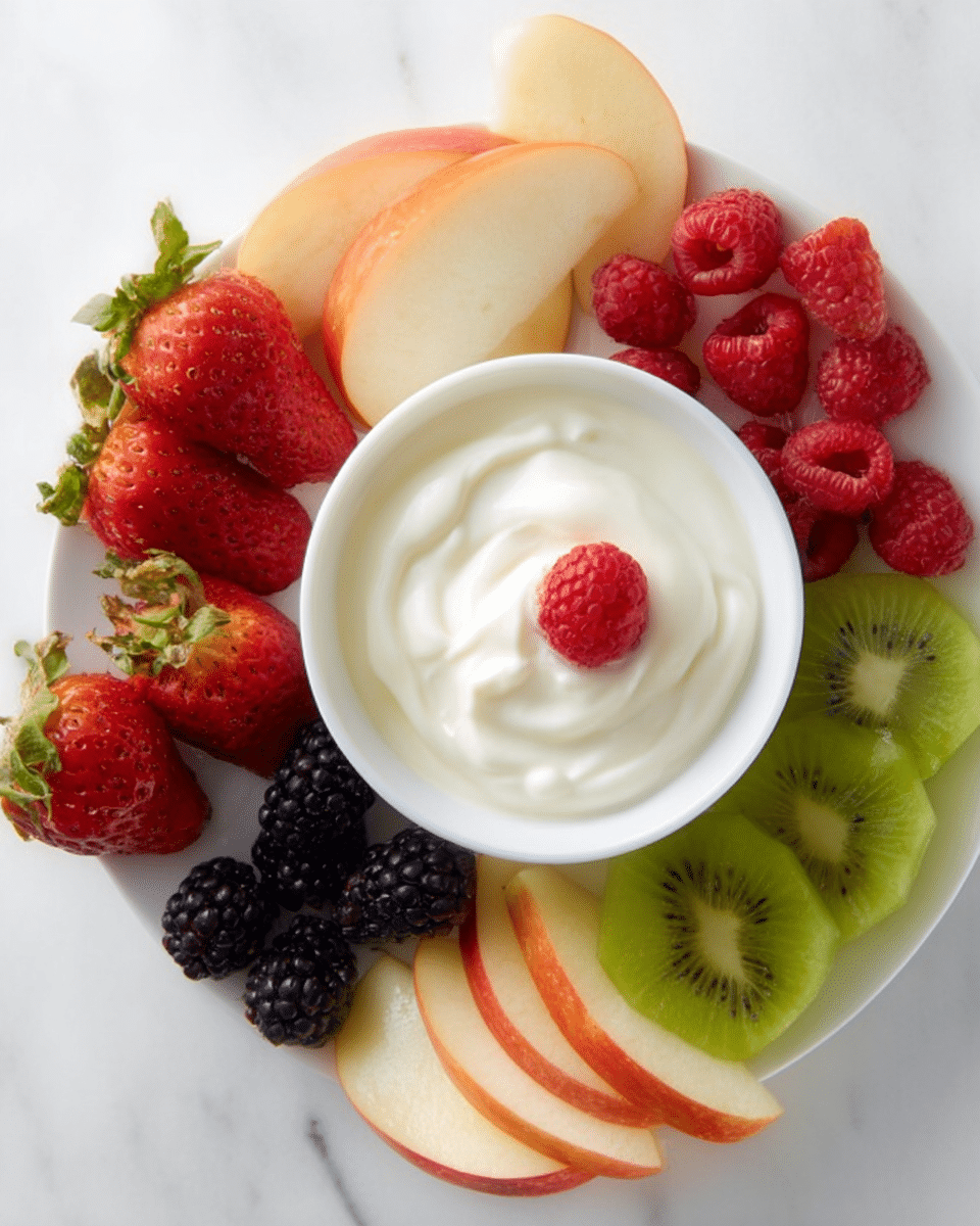 A white plate on a white marbled surface holds a small white bowl filled with smooth, white yogurt topped with a single red raspberry. Around the bowl, there are fresh fruit slices and whole fruits arranged in groups: bright red strawberries with green leaves, several apple wedges with red skin and pale yellow flesh, thin round slices of green kiwi with dark seeds, whole blackberries, and a few scattered red raspberries adding pops of color. The fruits are placed next to each other forming a colorful circular pattern around the yogurt bowl. Photo taken with an iphone --ar 4:5 --v 7