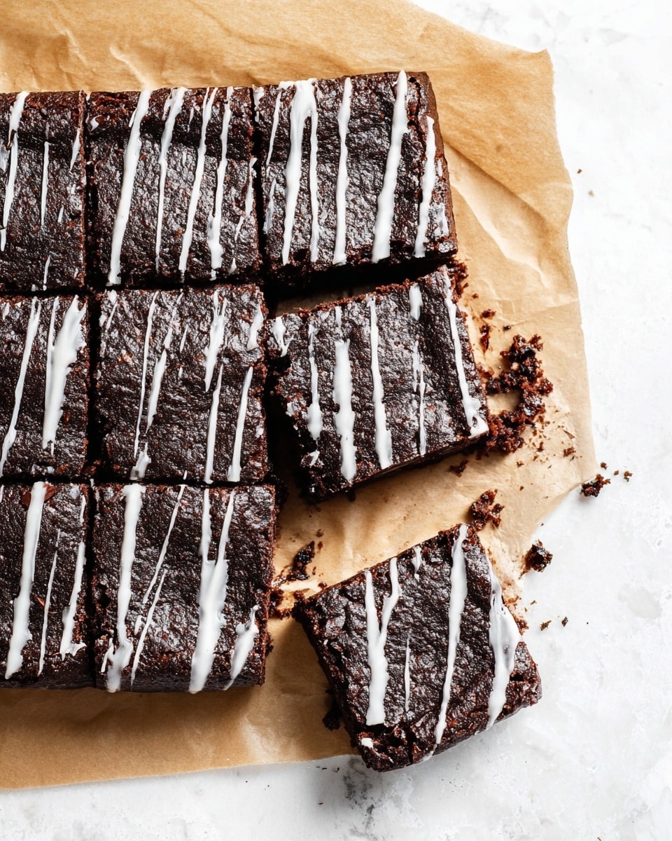 A dark chocolate brownie cut into nine square pieces sits on a sheet of brown parchment paper over a white marbled surface. The brownies have a slightly rough texture with visible cracks on the surface, and each piece is topped with thin, uneven white glaze lines drizzled across horizontally. One brownie piece is pulled slightly away from the main block, showing its dense but moist inside, and there are small crumbs scattered around it. The contrast between the dark brown of the brownies and the white glaze highlights the rich, fudgy texture. Photo taken with an iphone --ar 4:5 --v 7