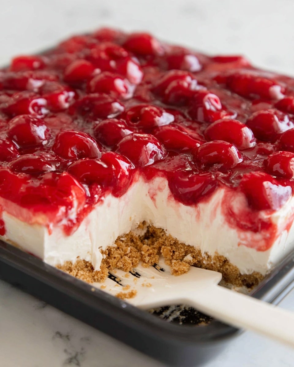 The image shows a close-up of a cherry dessert in a black baking tray. The dessert has three clear layers: the bottom layer is a crumbly light brown crust, the middle layer is a smooth, creamy white filling with a few crumbs stuck in it, and the top layer is a bright red cherry topping with whole cherries covered in a shiny glaze. A white spatula is partially under the dessert, with some crumbs and filling on it. The scene is set on a white marbled texture. photo taken with an iphone --ar 4:5 --v 7