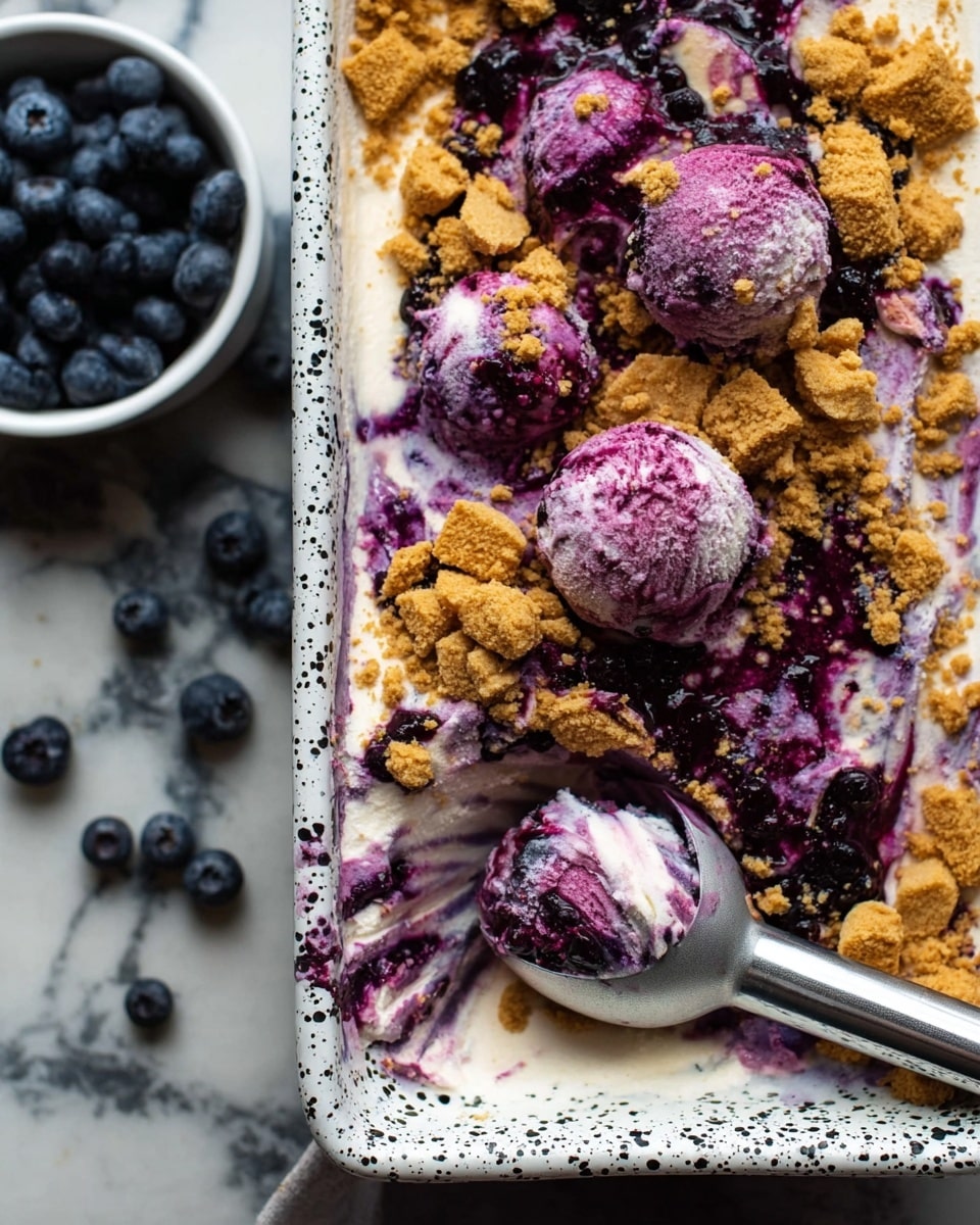 A close-up of a dessert in a rectangular white tray with black spots, showing a mix of colors and textures. The bottom layer looks creamy white ice cream with a smooth texture. On top, there is a thick layer of purple blueberry sauce mixed throughout, giving a swirled look. Over the sauce, there are crumbled golden-brown cookie pieces scattered unevenly in chunks. A metal ice cream scoop with purple stains is scooping out several round balls of the ice cream and sauce mix. Part of a white bowl with fresh blueberries sits beside the tray, all placed on a white marbled surface. Photo taken with an iphone --ar 4:5 --v 7