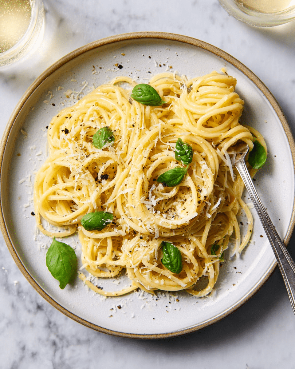 A white plate holds a twisting nest of yellow spaghetti noodles coated in a light sauce. Scattered finely grated white cheese and cracked black pepper rest on top, adding texture and specks of color. Bright green basil leaves are placed evenly over the strands, offering a fresh contrast to the pasta's pale yellow. A fork is twirling a small bunch of noodles on the right side of the plate. The plate sits on a white marbled surface with a glass of light-colored drink next to it. photo taken with an iphone --ar 4:5 --v 7
