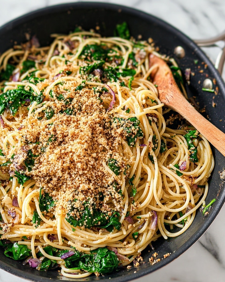 A close-up view of a black cooking pan filled with a pile of light yellow spaghetti mixed with bright green leafy spinach and small bits of purple onion. The top layer is sprinkled with a thick, crumbly, golden brown breadcrumb topping. A wooden spoon sits inside the pan on the right, partially under the pasta, with some breadcrumbs and spinach around it. The pan rests on a white marbled surface. photo taken with an iphone --ar 4:5 --v 7