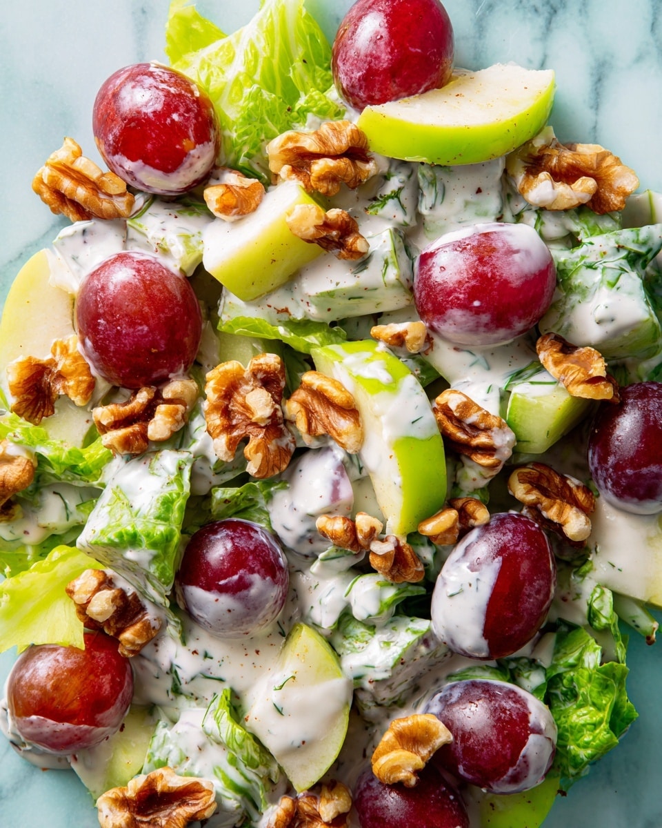 The image shows a close-up of a mixed salad with creamy dressing, featuring three main layers: creamy white dressing with herb specks spread evenly, vibrant red halved grapes with smooth skin and glossy texture, and crunchy light brown walnut pieces scattered throughout. There are also bright green celery slices, cut into curved shapes, and small chunks of pale yellow apple with red skin edges. The ingredients are densely packed, creating a mix of fresh, juicy, crunchy, and creamy textures on a white marbled surface. photo taken with an iphone --ar 4:5 --v 7