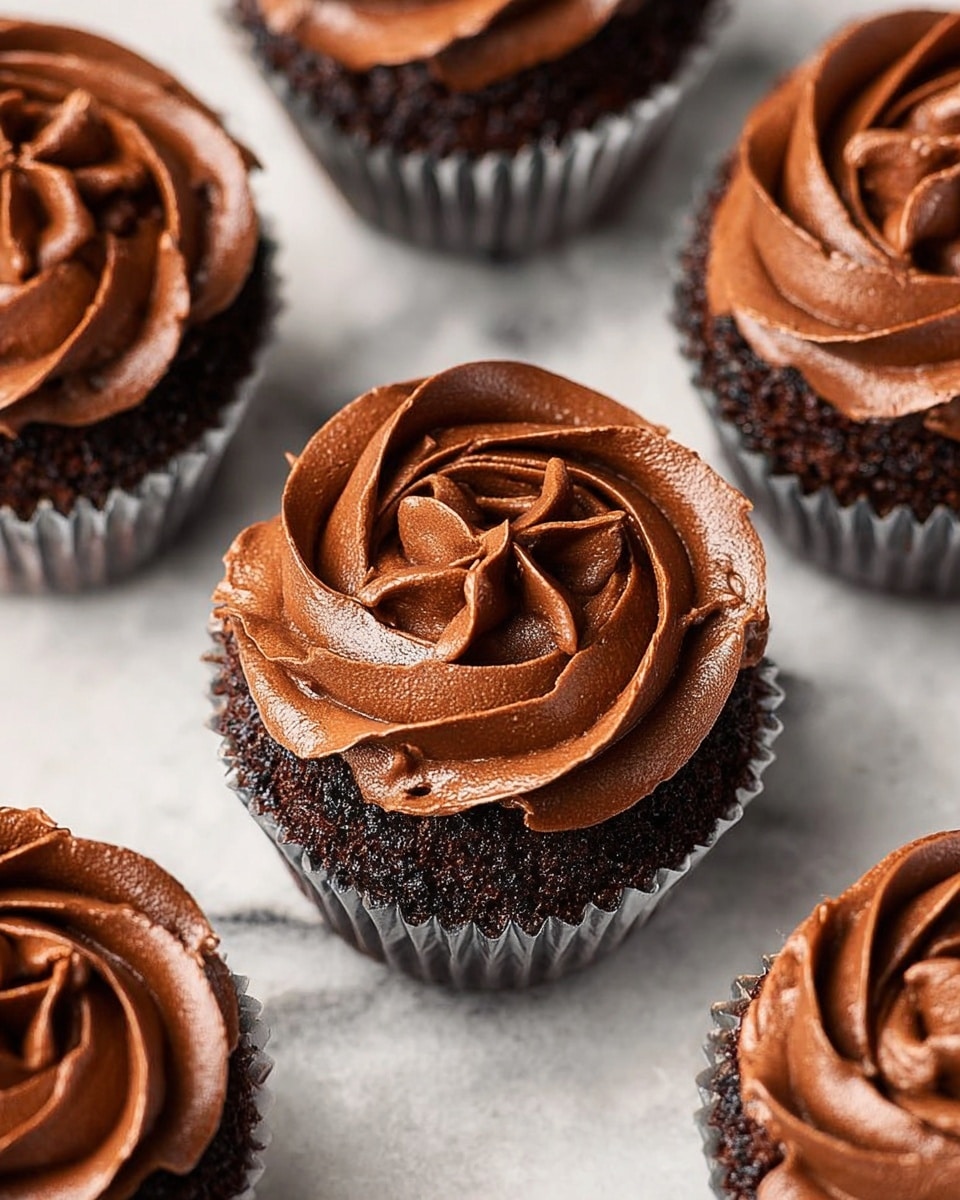 A white bowl filled with thick, creamy chocolate frosting, showing soft waves and swirls with a smooth, shiny texture. Next to the bowl, on a white marbled surface, lies a red spatula with some chocolate frosting spread unevenly on its edge. The frosting is a rich brown color, smooth and fluffy, filling the bowl almost to the top, creating a sense of depth and softness. The scene is simple and focused on the rich texture of the chocolate frosting. photo taken with an iphone --ar 4:5 --v 7