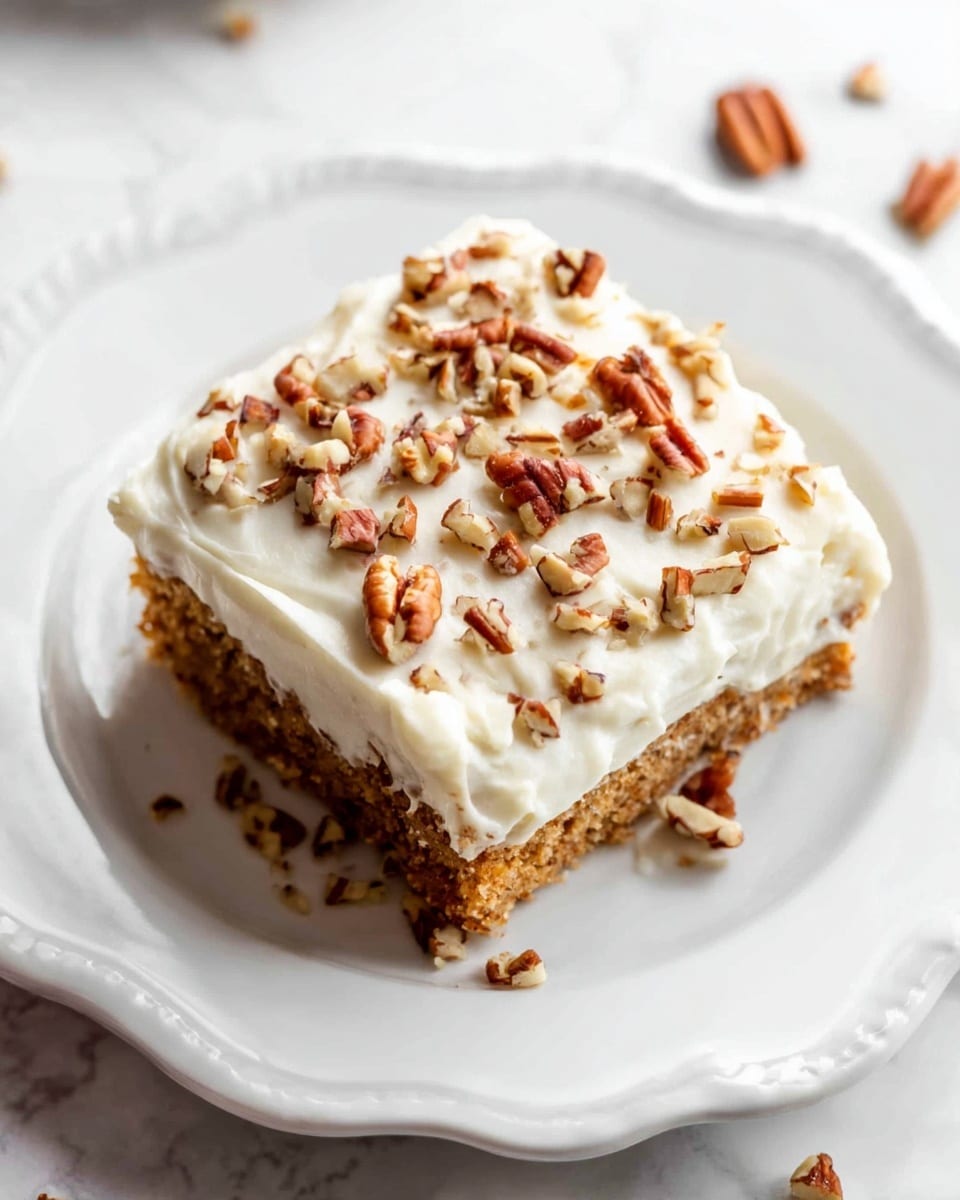 A square piece of cake sits in the center of a white plate with a scalloped edge. The cake has two visible layers: the bottom layer is a light brown, moist cake, while the top layer is a thick, creamy white frosting. The frosting is smooth but has some soft ridges and is sprinkled with chopped pecans in various sizes, adding texture and a mix of warm brown tones. Some small nut pieces are scattered on the plate near the cake. The background is a white marbled texture. photo taken with an iphone --ar 4:5 --v 7